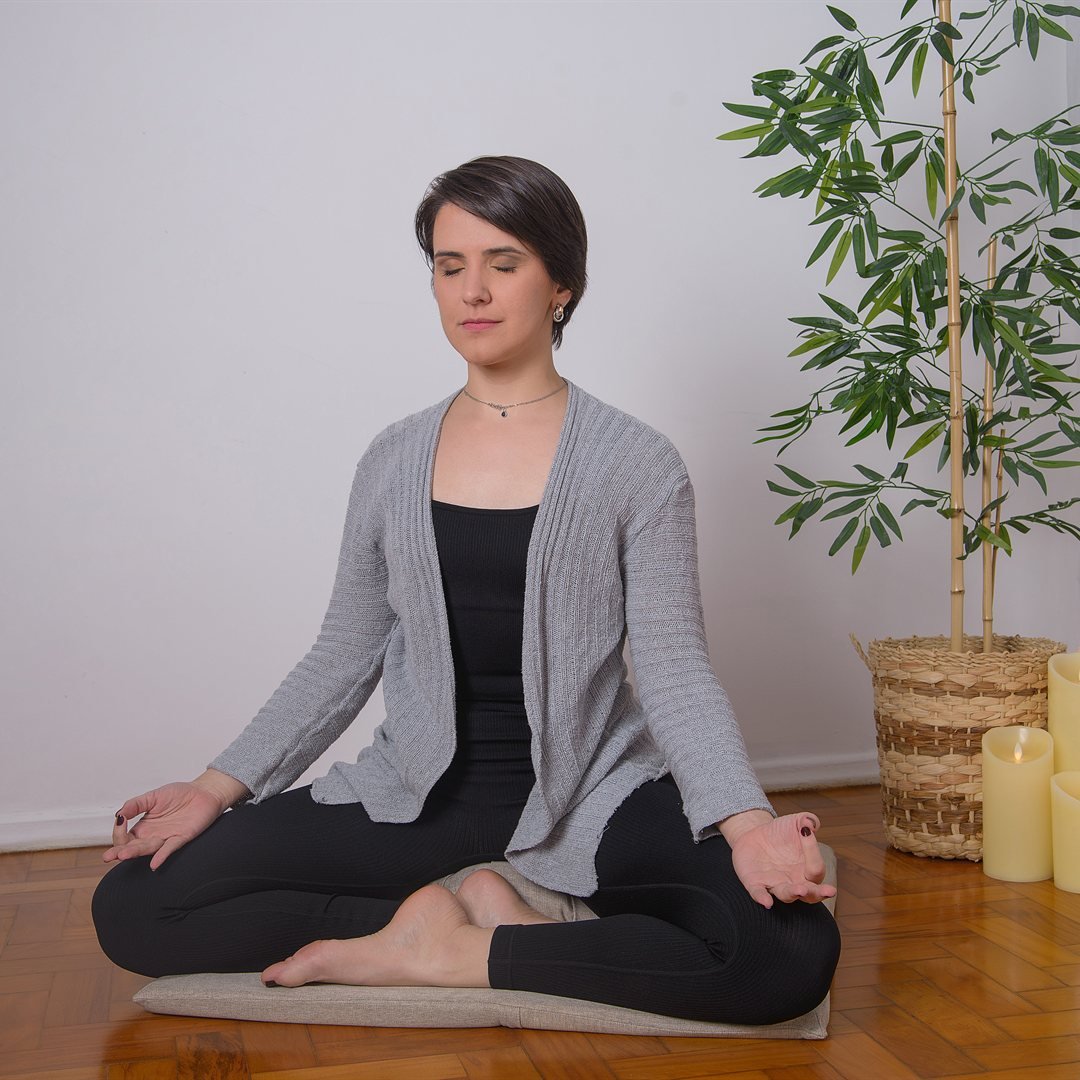 Nathalia em postura sentada de meditação, olhos fechados