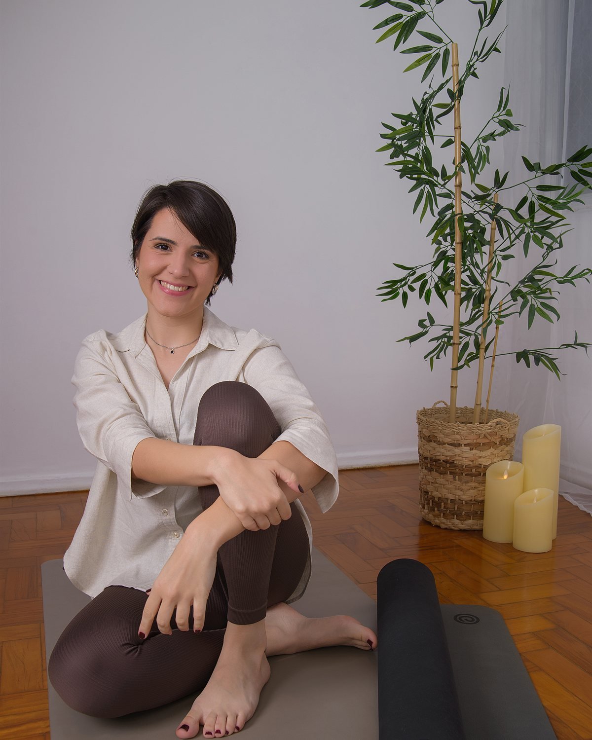 Nathalia Bedor sentada no tapete de yoga, sorrindo, com um bambu e velas ao fundo
